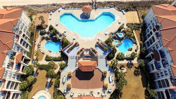 Oversigtsbillede af et resort med en hjerteformet pool, flere mindre pools og en central bygning med tagterrasse.