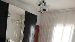 Makuuhuoneessa on vihreä, kuviollinen sängynpeite, suuri peili, kattotuuletin ja ikkuna, jossa on valkoiset verhot.
