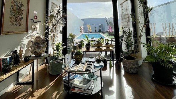 A spacious living room with a large window, a pool view, and various plants. - Praia de Santos, Exclusive Villa, Sea-sided with swimming pool, Azores Islands (São Roque)