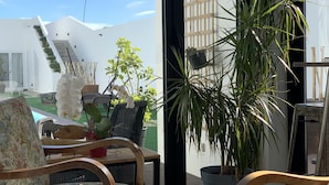 A modern outdoor seating area with wicker furniture, a potted plant, and a view of a white building with a staircase. - Praia de Santos, Exclusive Villa, Sea-sided with swimming pool, Azores Islands (São Roque)