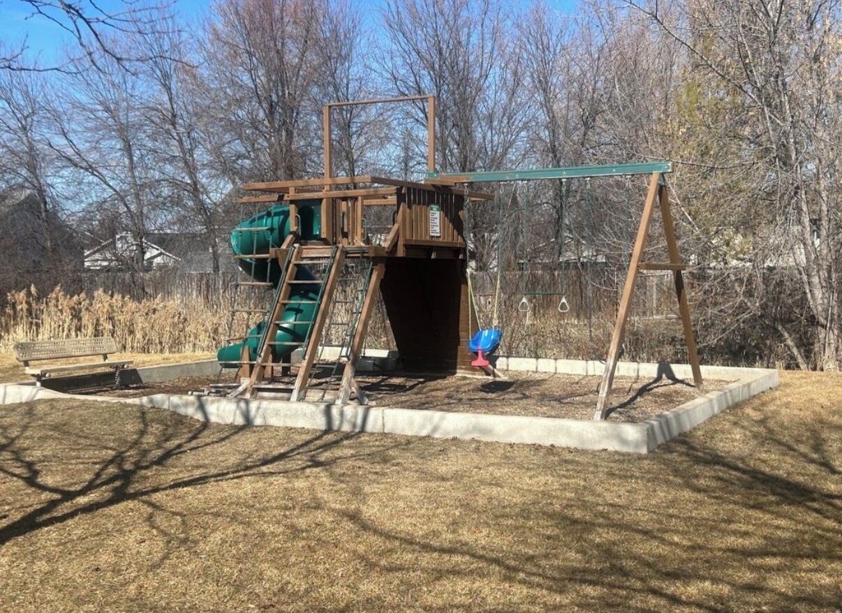 Une aire de jeux avec des balançoires, un toboggan et une structure d’escalade.