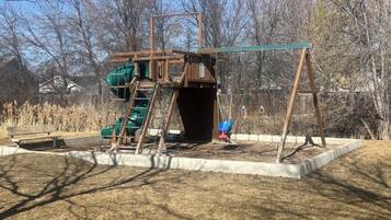 Une aire de jeux avec des balançoires, un toboggan et une structure d’escalade.