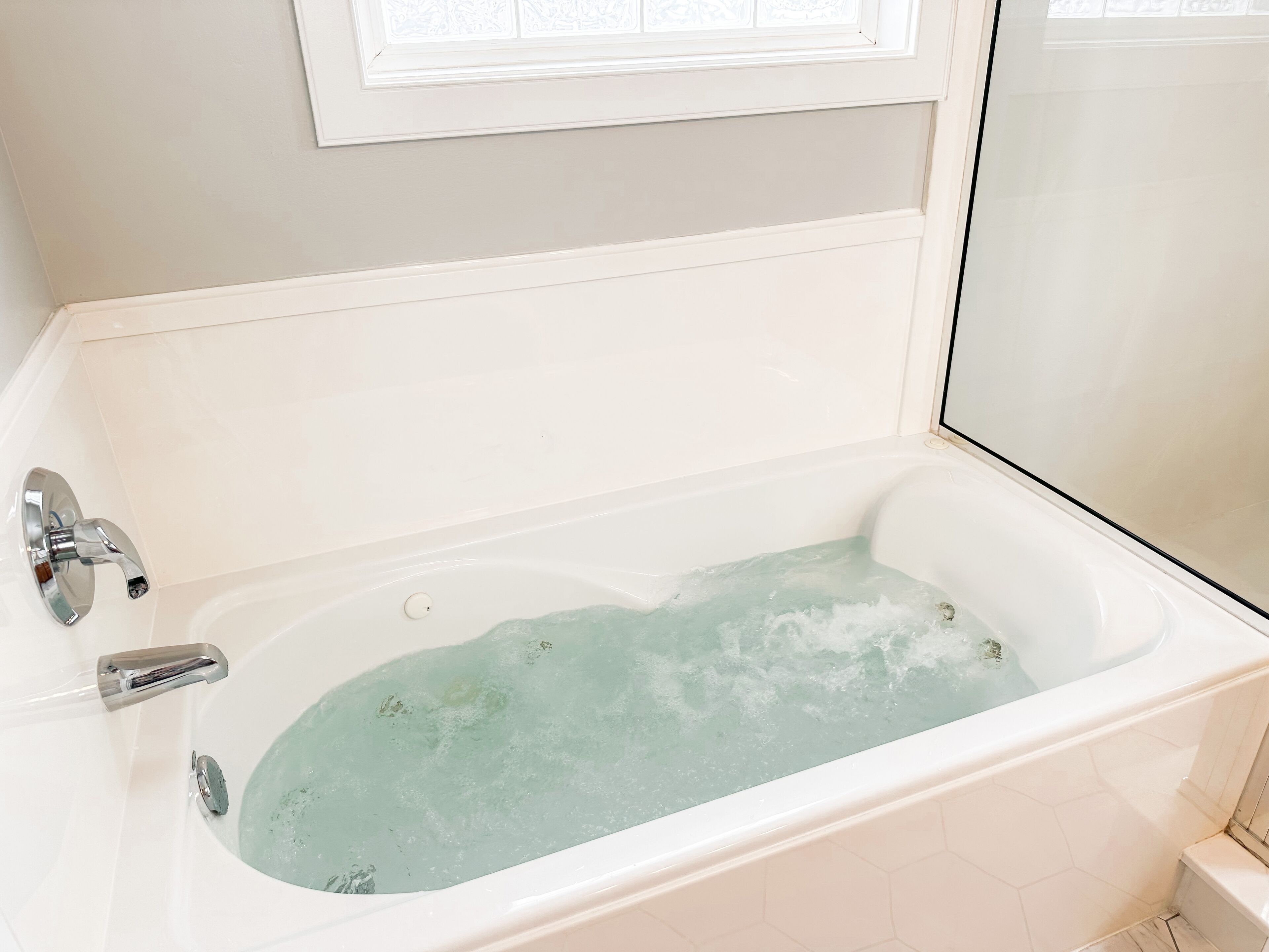 A white bathtub with running water, a chrome faucet, and a window above it.