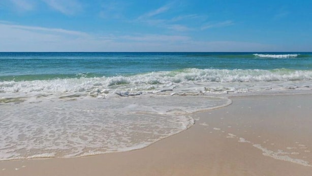 Una playa con cielos despejados y olas suaves.
