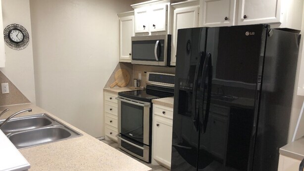 A kitchen with white cabinets, a black refrigerator, a microwave, an oven, and a sink. - Clean & Simple (Lubbock)