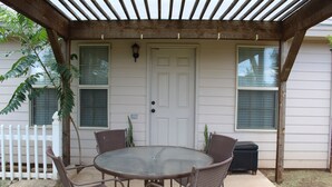 A covered patio with a round glass table and wicker chairs, a white door, and windows with blinds. - Clean & Simple (Lubbock)