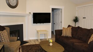 A living room with a fireplace, a television mounted on the wall, a sofa, and a coffee table with a vase of flowers. - Clean & Simple (Lubbock)