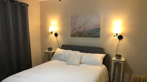 A neatly made bed with white linens, two bedside lamps, a painting on the wall, and a chair in the corner. - Clean & Simple (Lubbock)