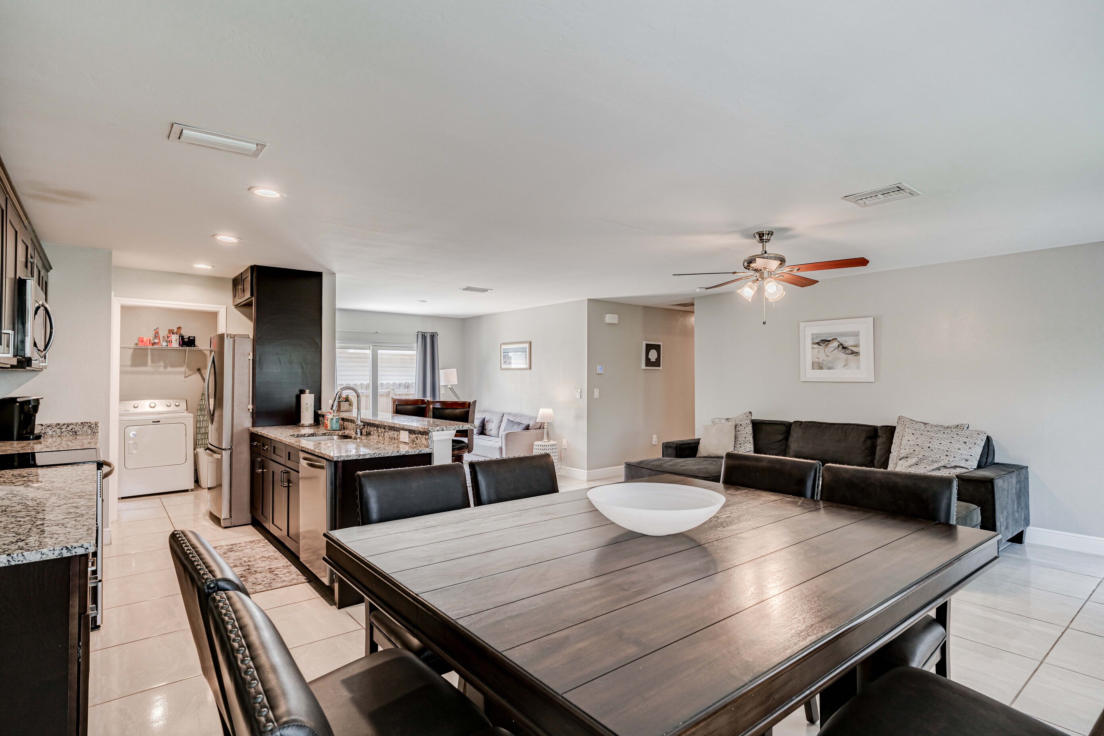 A modern kitchen with dark countertops, a large wooden dining table, and a built-in oven.