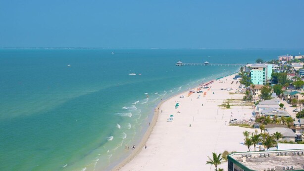 Ein Strand mit klarem türkisblauem Wasser, einer Pier und Gebäuden entlang der Küste.