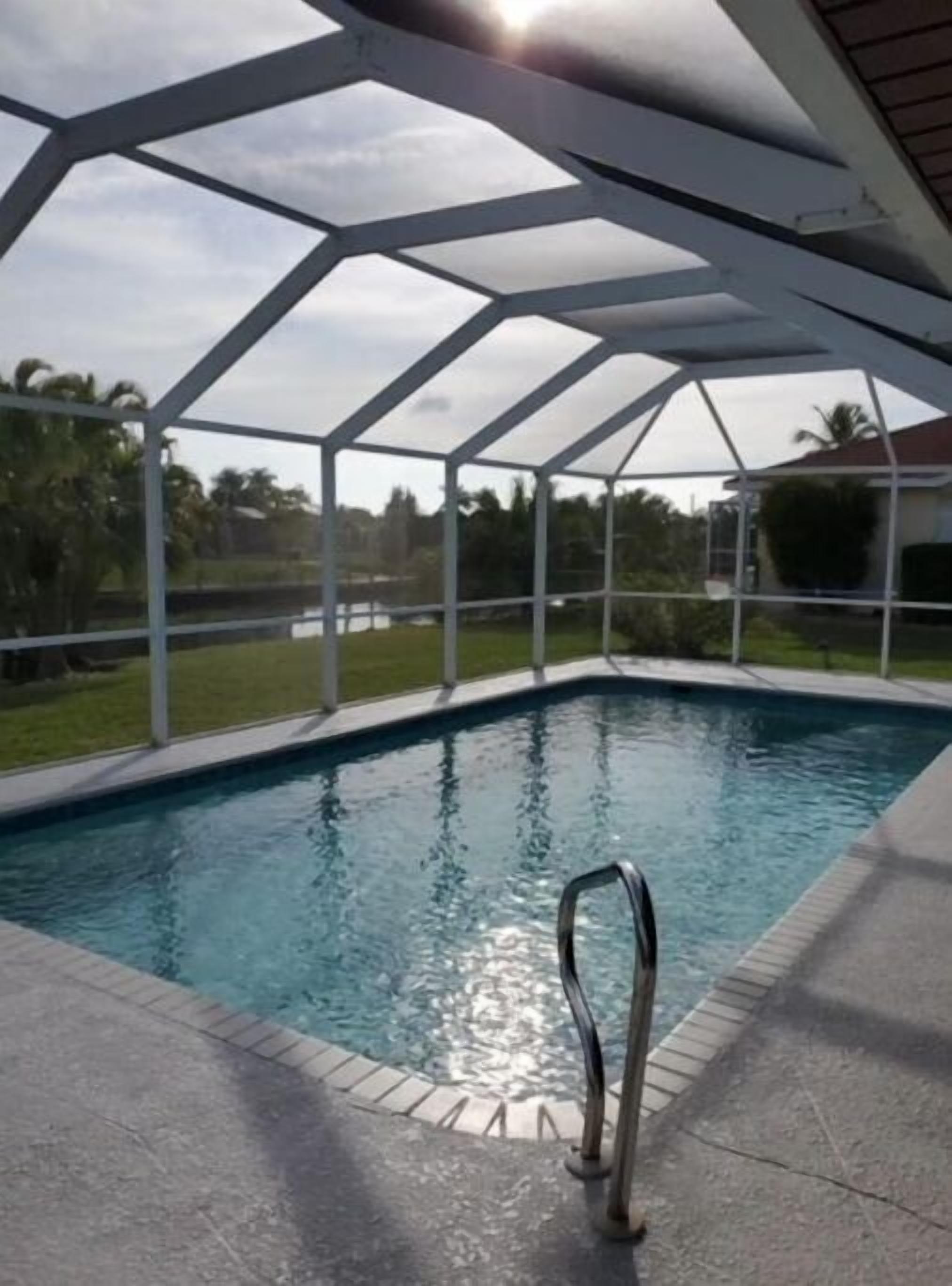 A swimming pool with a metal ladder, surrounded by a covered area with a geometric roof structure.