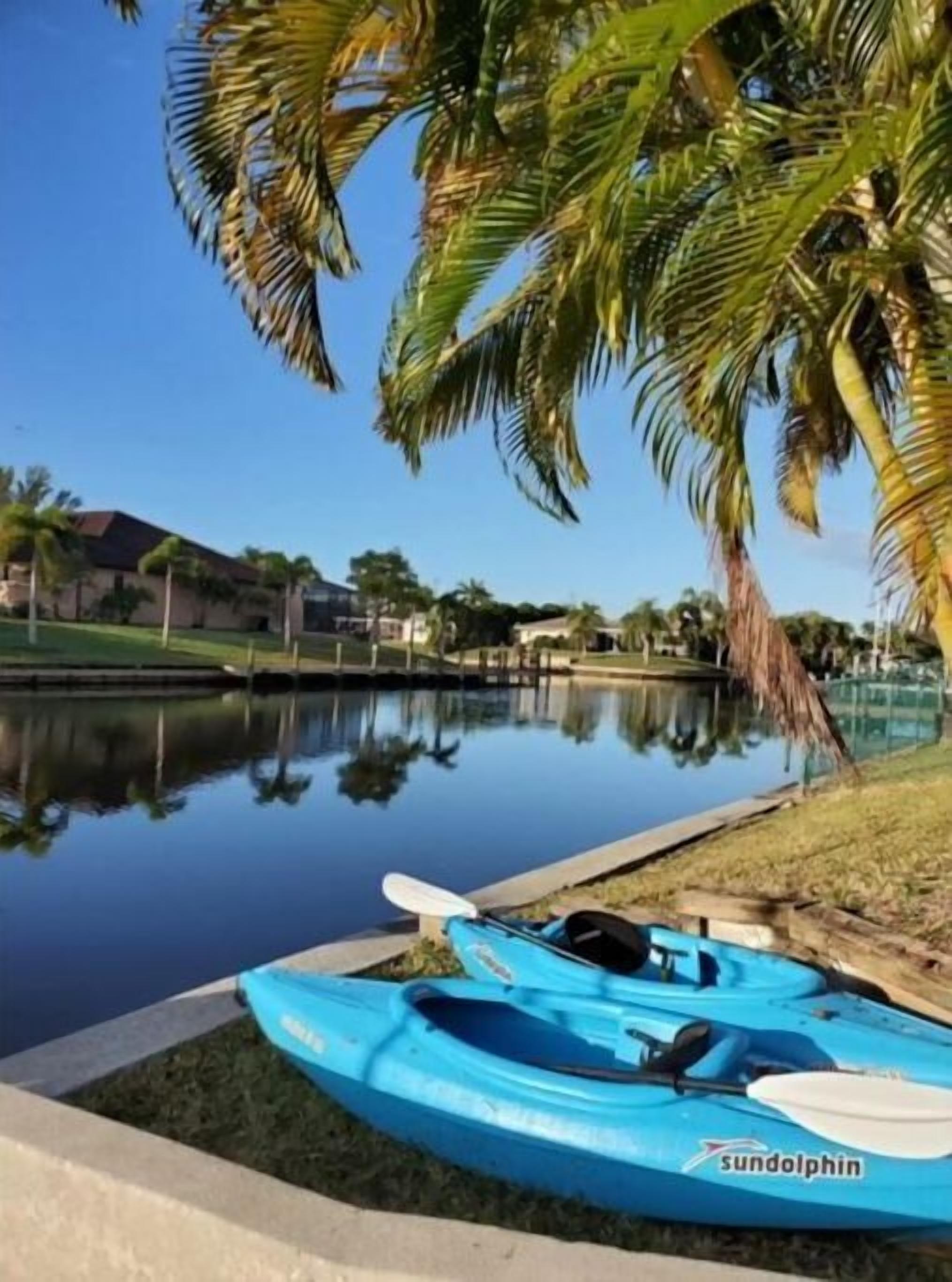 A calm water body with a kayak docked on the shore, surrounded by greenery and a clear sky.