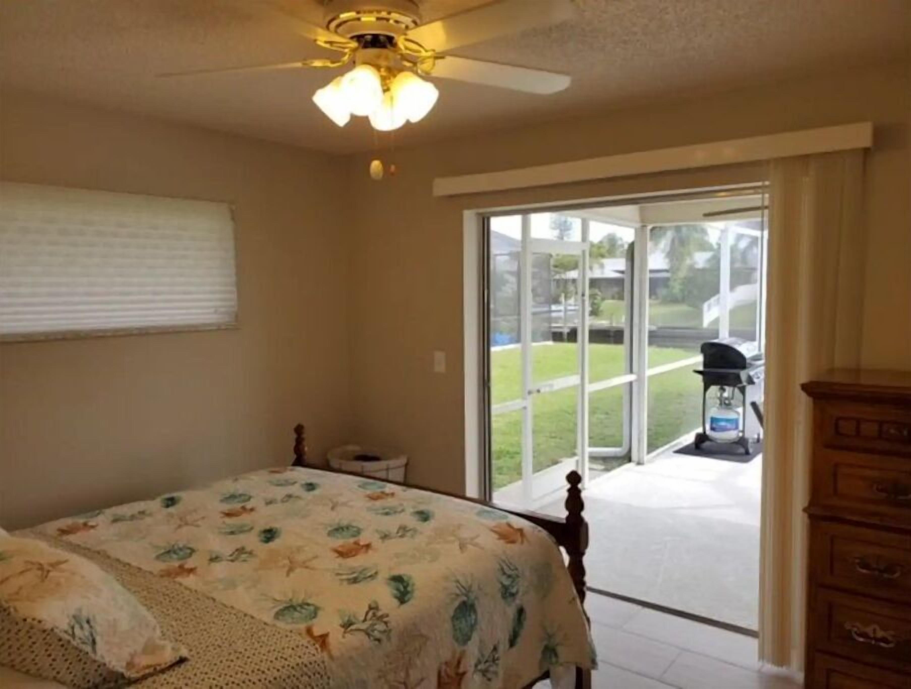 Un dormitorio con cama, ventilador de techo, ventana y vista al exterior.