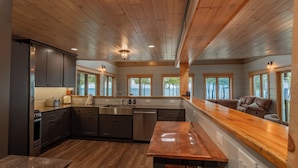 A modern kitchen with wooden flooring, a central island, and built-in appliances. - Bois Blanc Island Lighthouse Home. Iconic Sunset Views of the Mackinac Bridge! (Bois Blanc Island)