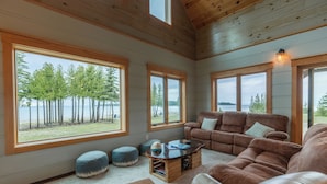 A cozy living room with large windows, a brown leather sofa, and a wooden coffee table. - Bois Blanc Island Lighthouse Home. Iconic Sunset Views of the Mackinac Bridge! (Bois Blanc Island)