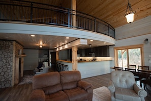 Relax in a spacious interior with a high ceiling and exposed beams. Enjoy the view from the curved balcony overlooking the kitchen area with modern appliances and bar stools.