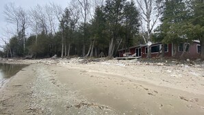 A cabin with a patio area, surrounded by trees and a sandy beach. - Waterfront gem, sandy beach, modern kitchen, large great room, free firewood (Sturgeon Bay)