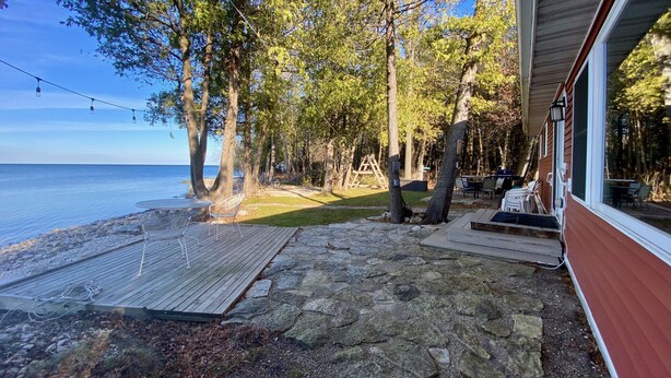A wooden deck leading to a stone patio with a view of the sea. - Waterfront gem, sandy beach, modern kitchen, large great room, free firewood (Sturgeon Bay)