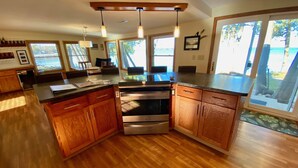 A modern kitchen with wooden cabinets, stainless steel appliances, and large windows offering a view of the outdoors. - Waterfront gem, sandy beach, modern kitchen, large great room, free firewood (Sturgeon Bay)
