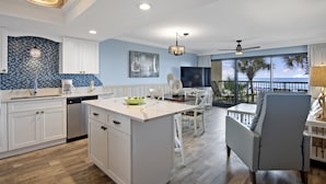 Una cocina moderna con armarios blancos, una isla central y un comedor con vista al océano.