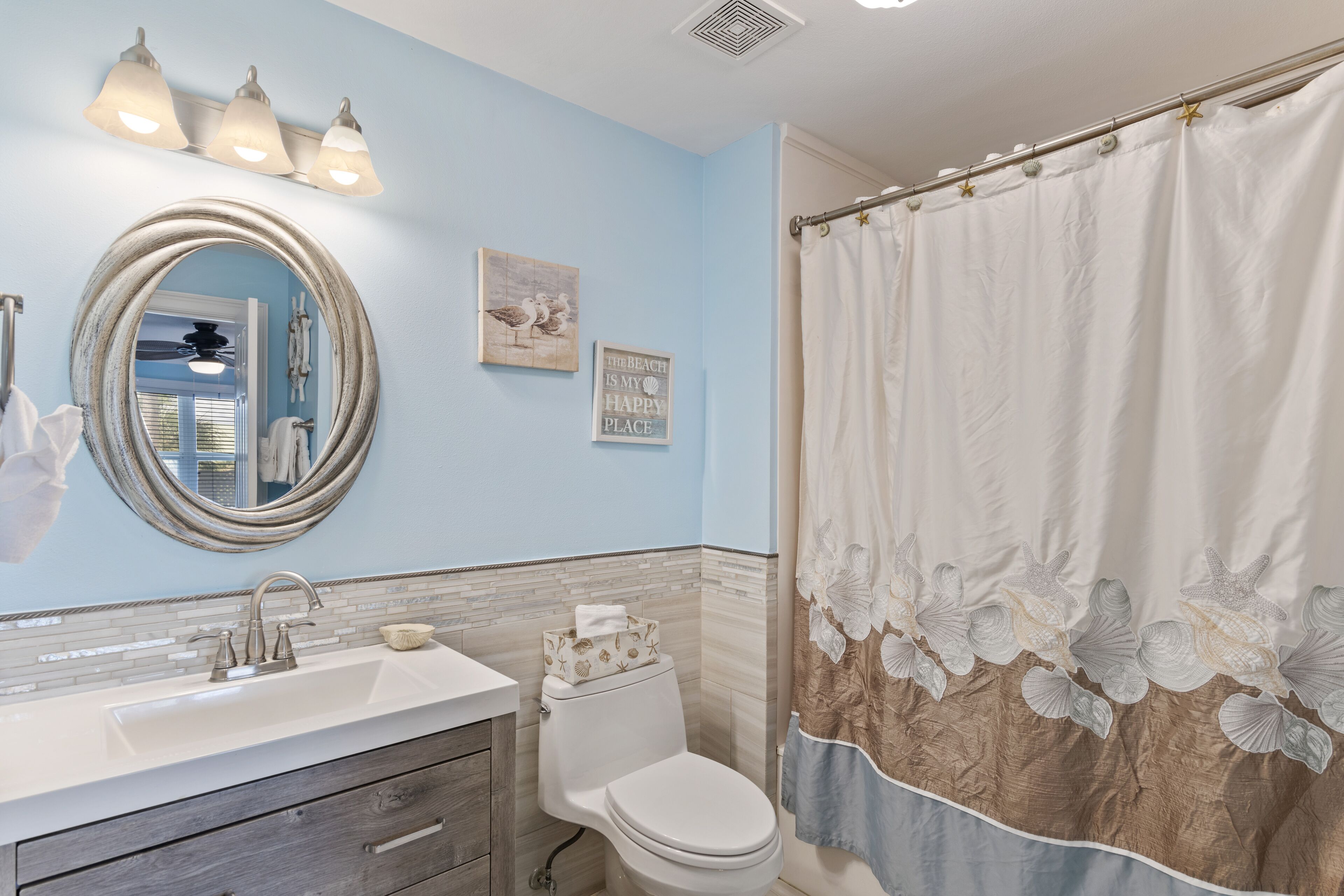 A bathroom with a white sink, a round mirror, a toilet, and a shower curtain with floral designs.