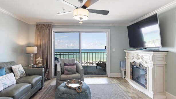 A living room with a sofa, armchair, ottoman, television, fireplace, and a balcony with a view of the ocean. - Newly Renovated Condo 305, Your Luxurious BEACH FRONT Paradise - Crystal Dune (Destin)