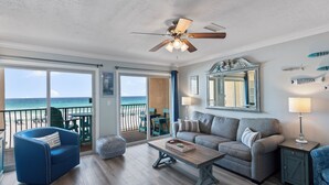 Un salon spacieux avec vue sur l’océan, doté d’un ventilateur de plafond, d’un canapé, d’une table basse et d’une table d’appoint avec une lampe.