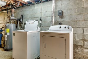 A laundry room with two washing machines, a water heater, and a vent pipe.