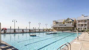 A swimming pool with clear blue water, surrounded by lounge chairs and umbrellas, and a building with balconies in the background.