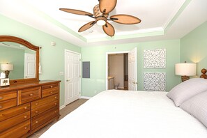 Une chambre à coucher comprenant un lit, une commode, un ventilateur de plafond et deux lampes fixées au mur.