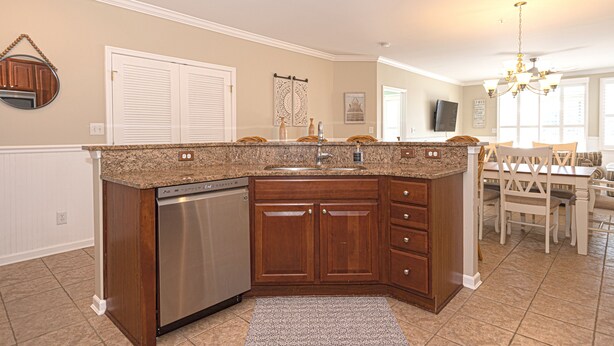 A kitchen with a dishwasher, wooden cabinets, a granite countertop, and a dining area with a table and chairs.