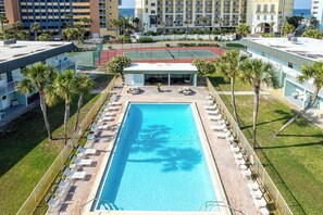 Relax by the rectangular pool surrounded by sun loungers and umbrellas, with a tennis court nearby.