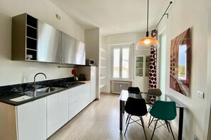 Une cuisine moderne avec des meubles blancs, un plan de travail noir et un coin repas comprenant une table en verre et deux chaises.