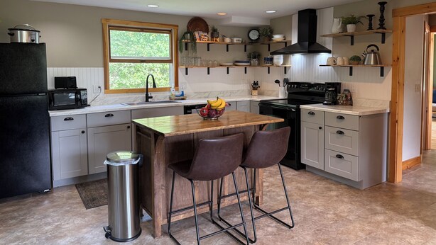 A modern kitchen with a wooden island, bar stools, a sink, and a stove.