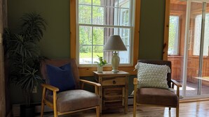 A cozy room with wooden flooring, two armchairs, a small table with a lamp, and a potted plant.
