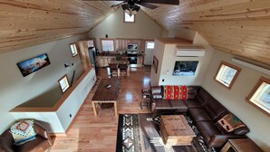 A spacious loft with a high ceiling, wooden beams, a dining area, a living room with a sofa and coffee table, and a kitchen with wooden cabinets. - Yellowstone Beauty Overlooking Yellowstone River BRAND NEW Gardiner, MT  (Gardiner)