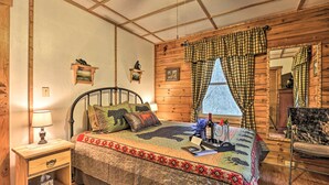 Ein gemütliches Schlafzimmer mit Holzbalkendecke, einem Bett mit gemustertem Überwurf, einem Nachttisch mit Lampe und einem Sessel.