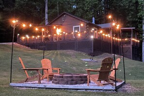 A wooden cabin with a deck, surrounded by a fence, and featuring two Adirondack chairs and a fire pit. - Hillside: Cosby 'Cozy Cove' Cabin w/ Hot Tub (Cosby)