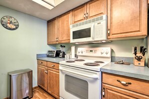 Kitchen area with a stove, refrigerator, and toaster, featuring a nautical-themed clock on the wall.
