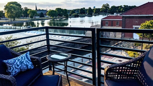 A balcony with a view of a river, a waterfall, and a church in the background. - Swanky Downtown Loft (Waverly)