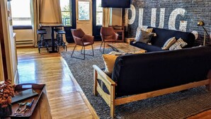 A cozy living room with a black sofa, two brown leather chairs, a wooden coffee table, and a large TV mounted on a brick wall. - Swanky Downtown Loft (Waverly)