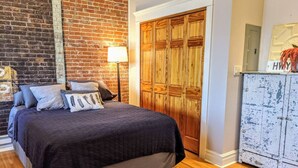 A bedroom with a bed, a wooden wardrobe, a lamp, and a brick wall. - Swanky Downtown Loft (Waverly)
