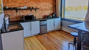 A modern kitchen with a brick wall, white cabinets, and a view of a lake through a large window. - Swanky Downtown Loft (Waverly)