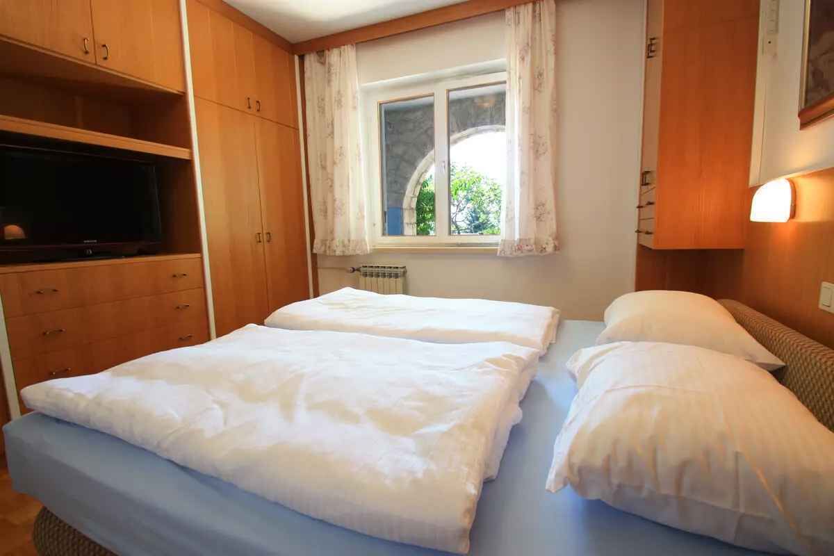A bedroom with two beds, wooden cabinets, a window with curtains, and a wall-mounted light.
