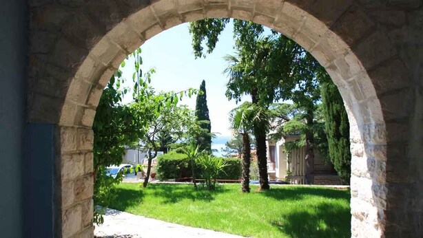 An arched stone doorway leading to a grassy area with trees and a statue.