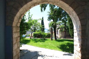 An arched stone doorway leading to a grassy area with trees and a statue. - Holiday apartment with a large terrace for sole use (Crikvenica)