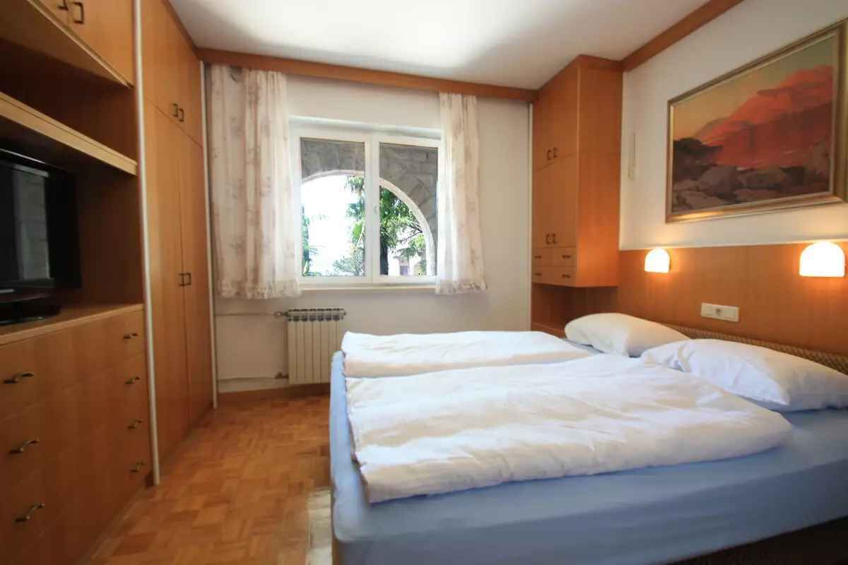 Une chambre avec deux lits, une fenêtre avec des rideaux, un radiateur, des armoires en bois et un tableau au mur.