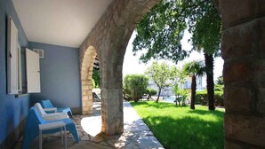 A stone archway leading to a patio with blue lounge chairs and a stone floor.