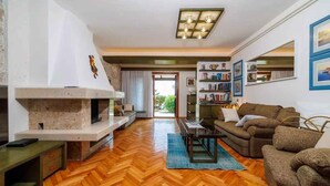 A spacious living room with a herringbone wood floor, a fireplace, a sofa set, a coffee table, and a bookshelf.