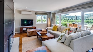 Un saló modern amb un gran televisió plana, seients confortables i vista a un paisatge exuberant a través de grans finestres.